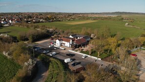 An aerial view of a rural hotel with a parking lot, a small garden, and a view of the surrounding countryside. - The Ferry Boat Inn (Chelmsford)
