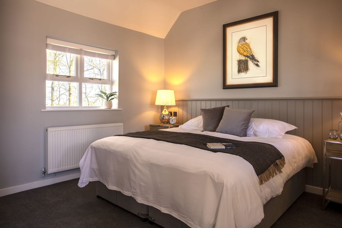 A neatly made bed with white linens, a bedside lamp, and a framed bird painting on the wall.