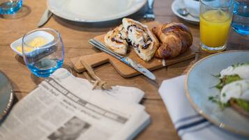 Esmorzar amb croissants, un got de suc d'aranja, un plat de menjar i un diari sobre una taula de fusta.