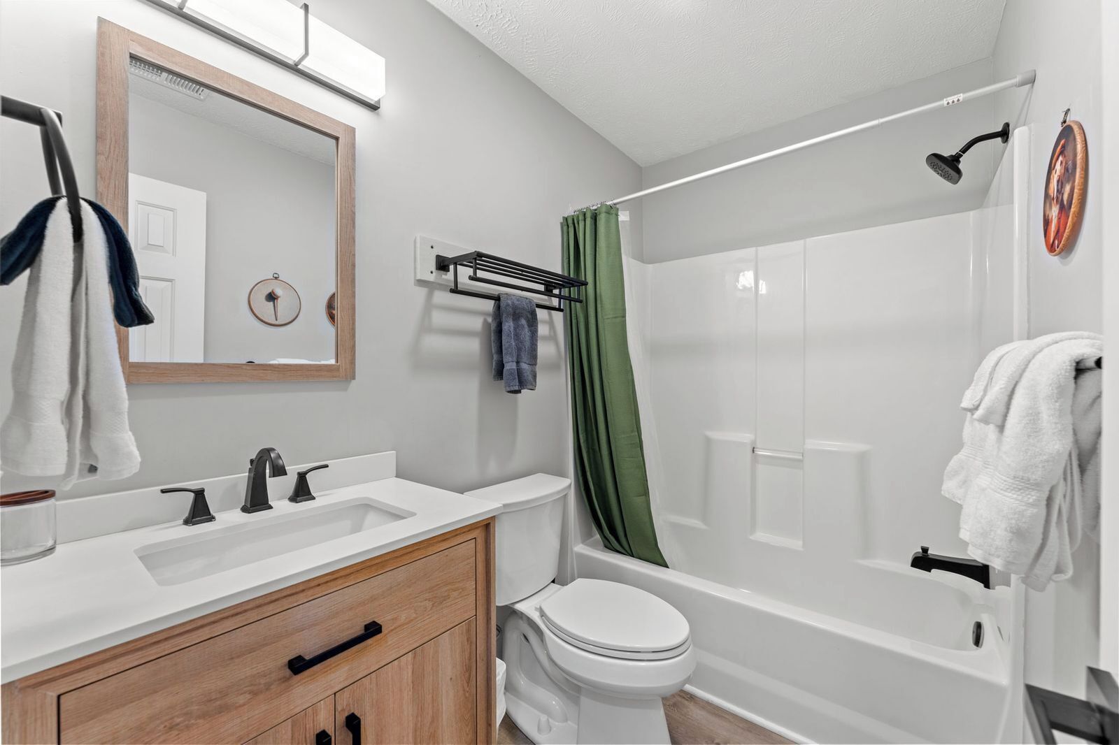 A modern bathroom with a white sink, vanity, and toilet. There is a shower with a green curtain and a handheld showerhead.