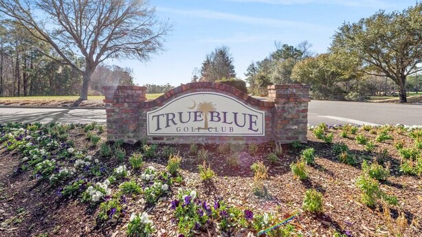 Une enseigne indiquant l’entrée du True Blue Golf Club, entourée de parterres de fleurs aménagés.