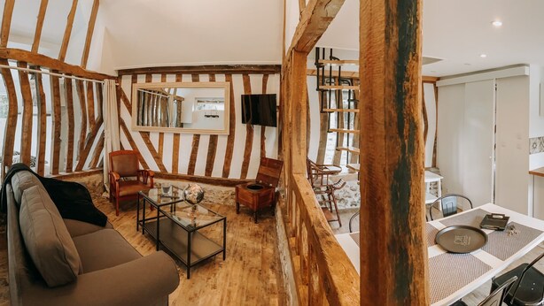 Een ruime woonkamer met houten plafond, een eettafel met stoelen, en een keuken met witte kastjes en een koelkast.