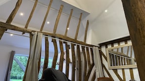 Een kamer met zichtbare houten balken, een plafondlamp en uitzicht op groen.
