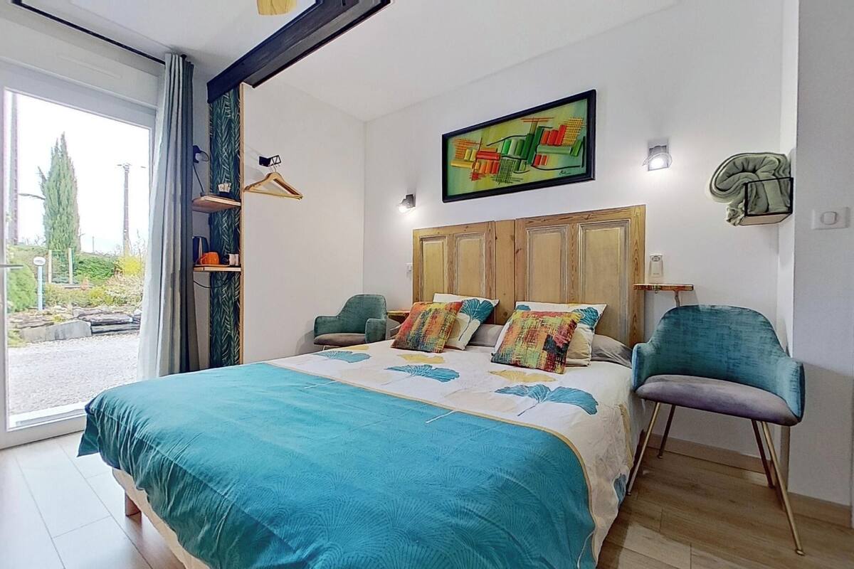 A bedroom with a large bed, a wooden headboard, a painting, a chair, and a view of the outdoors.