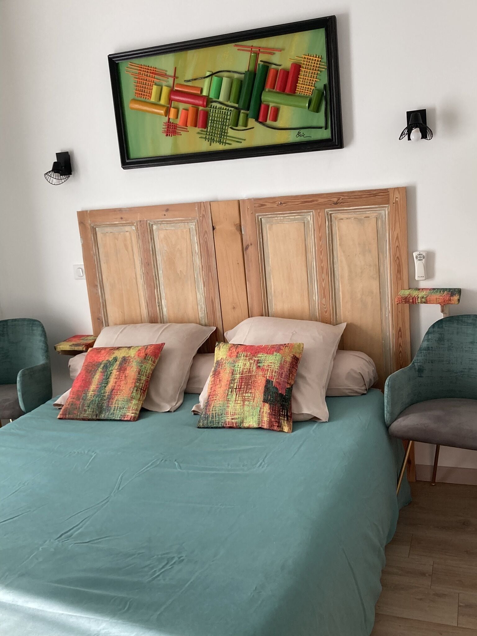Un dormitorio con cabecera de madera, colcha color turquesa y dos almohadas coloridas.