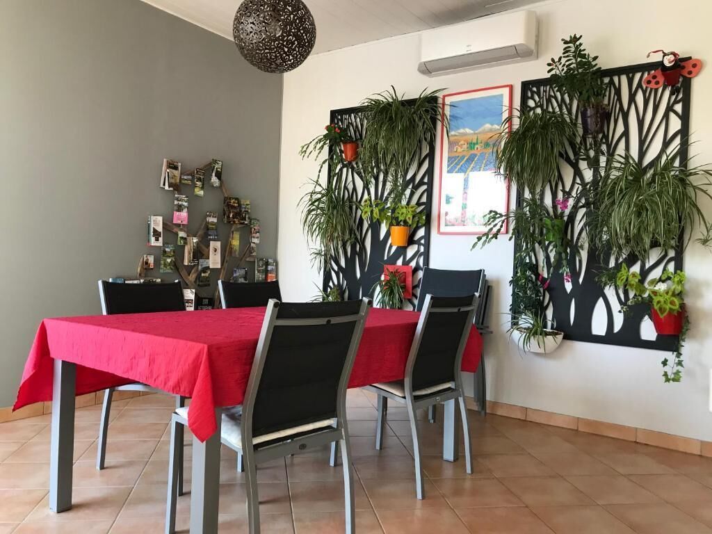 Comedor con mantel rojo, sillas negras y una pared decorativa con plantas.