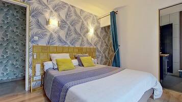 A modern bedroom with a patterned wallpaper, a wooden headboard, a bed with striped bedding, and a bathroom visible through an open door.