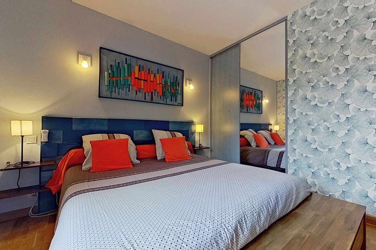 A modern hotel room with a large bed, a blue headboard, and a large mirror.