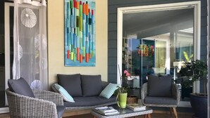 A patio area with wicker furniture, a glass door, and a colorful abstract painting. - Escale En Correze (Sadroc)