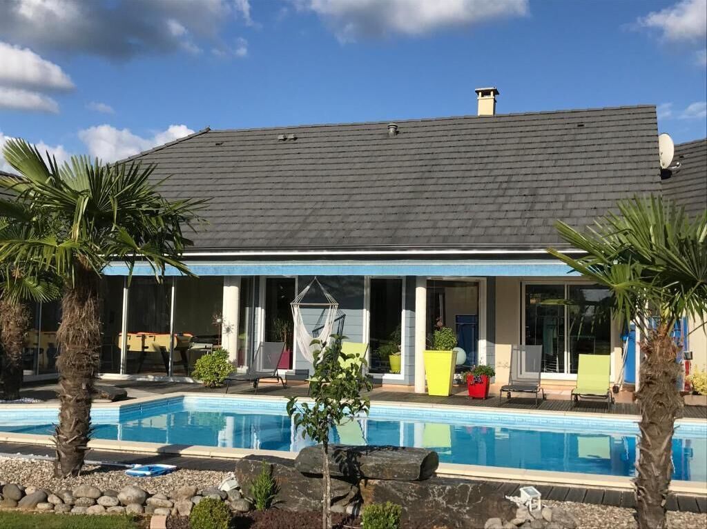 A modern house with a swimming pool, a covered patio, and palm trees.