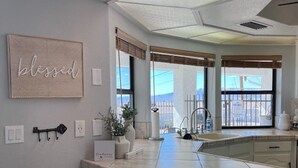 Une cuisine dotée d’un grand îlot central, de deux tabourets de bar, d’une pancarte portant l’inscription « béni » et offrant une vue sur l’extérieur.
