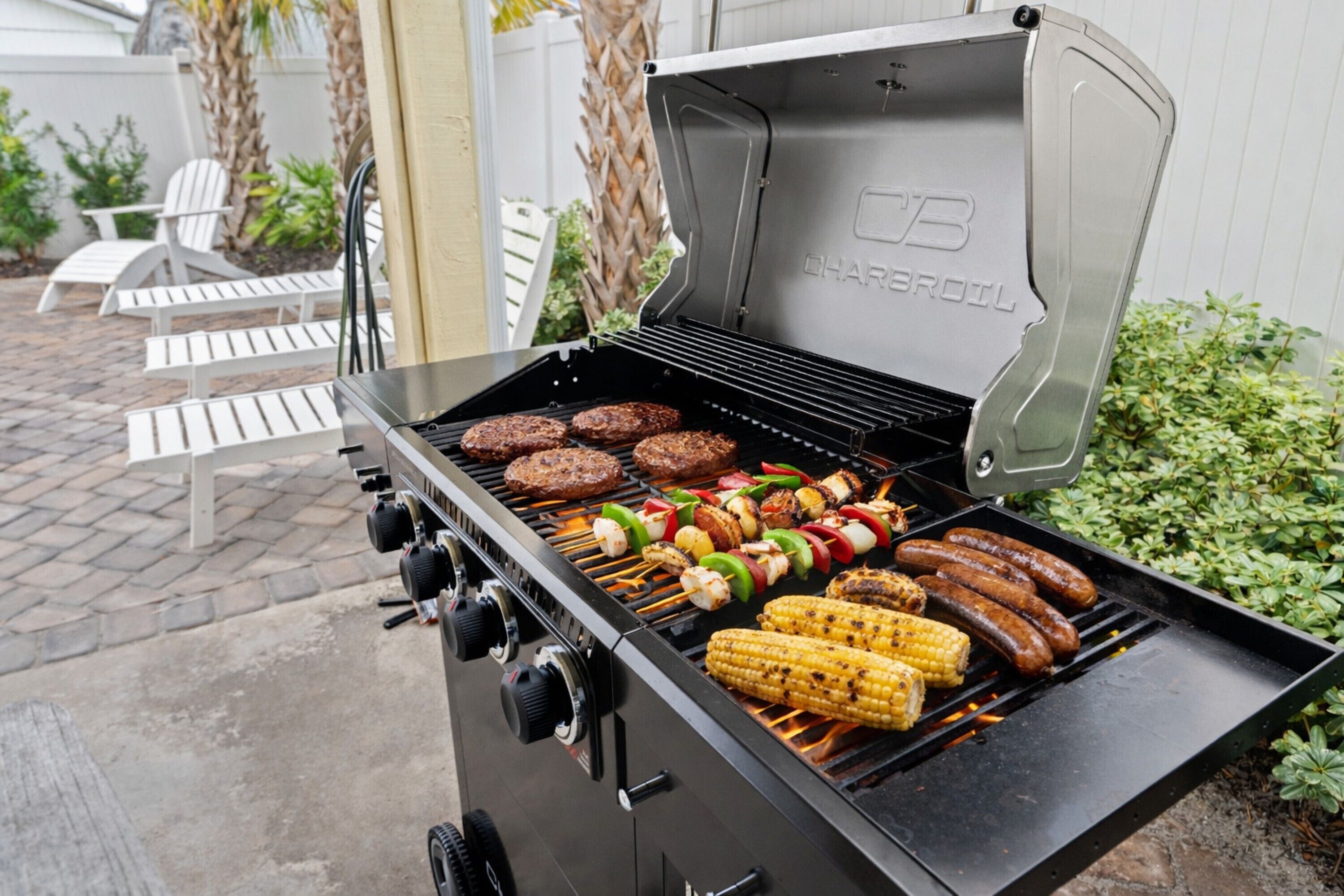 Ein Holzkohlegrill mit Hamburgern, Bratwürsten, Maiskolben und Spießen.