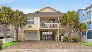 A two-story building with a balcony, a garage, and a paved driveway. - No Shoes, No Shirt, No Problems at this 4 Bed/3 Bath Home with Hot Tub - Walk to Beach (North Myrtle Beach)