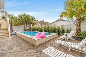 A backyard with a swimming pool, lounge chairs, and palm trees.