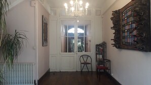 A hallway with a white door, a chair, a radiator, and a chandelier. - Magnificent and large 18th century house, in a mountain village (Luz-Saint-Sauveur)