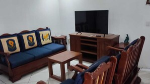 A living room with a sofa, a coffee table, a TV on a wooden stand, and a wooden chair. - Nice condominium with lots of amenities. Huatulco (Crucecita)