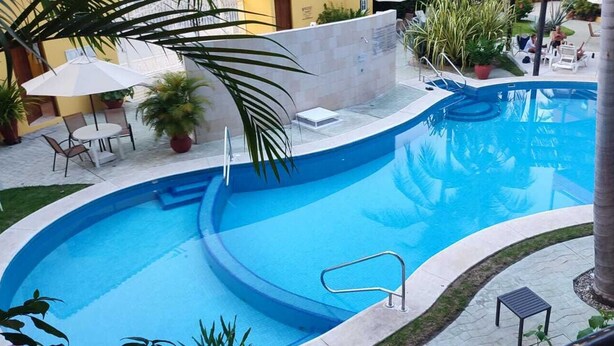 A curved swimming pool with a small deck area, surrounded by potted plants and a few lounge chairs. - Nice condominium with lots of amenities. Huatulco (Crucecita)