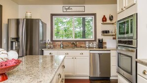 A modern kitchen with stainless steel appliances, a granite countertop, and a window with a view of trees.