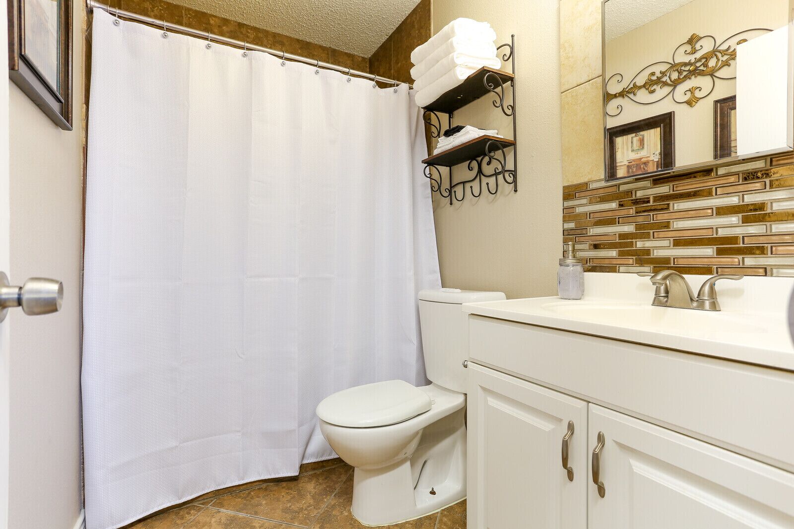 Une salle de bain équipée d’un rideau de douche, de toilettes, d’un lavabo et d’un miroir décoratif.