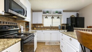 A modern kitchen with white cabinets, a black stove, a microwave, and a refrigerator. - Spacious Home with Pool Sleeps 10  Near Lackland BMT Graduation Family Friendly (San Antonio)
