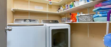 A laundry area with two washing machines, a fire extinguisher, shelves with cleaning supplies, and a microwave.