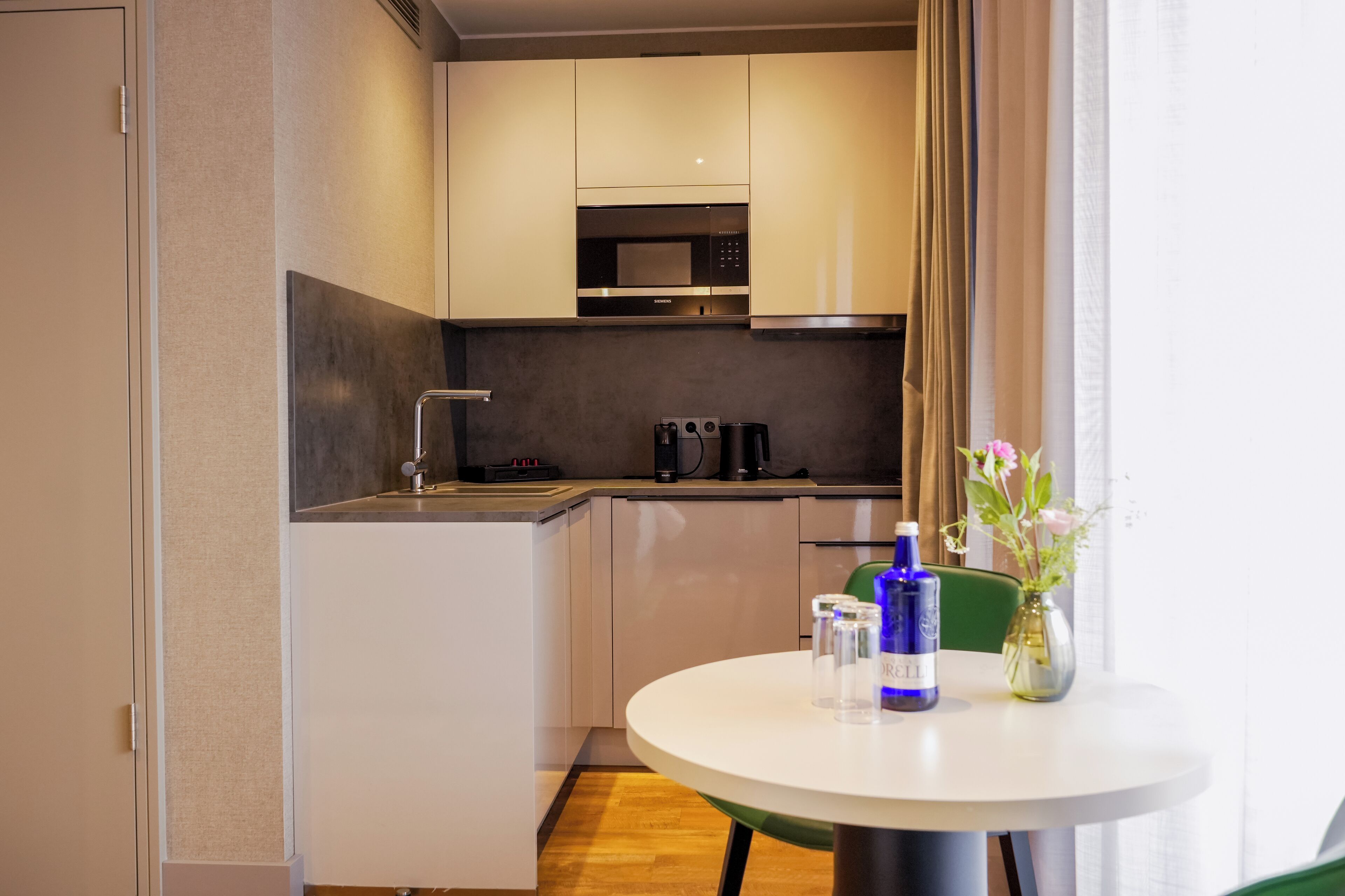 A compact kitchen with a microwave, coffee maker, and a small dining table with a vase of flowers.