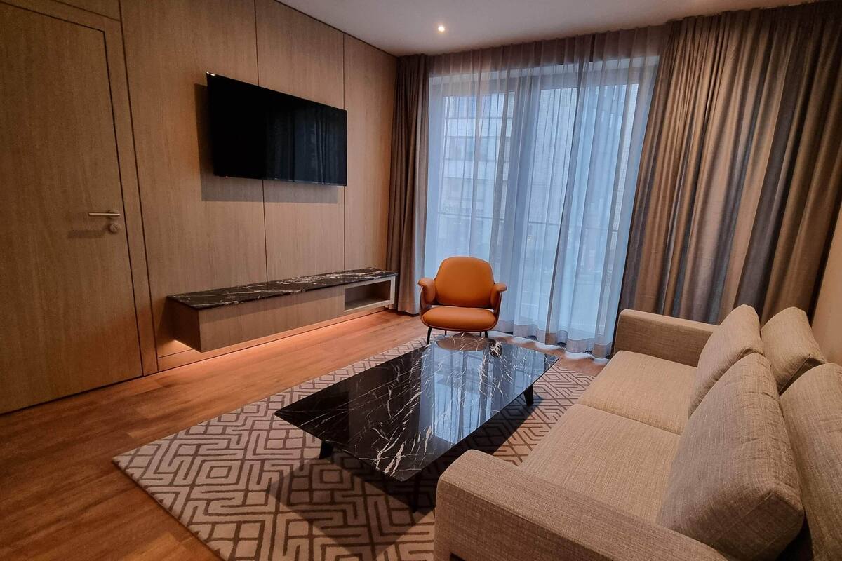 A modern living room with a sofa, a coffee table, a TV mounted on the wall, and a window with curtains.