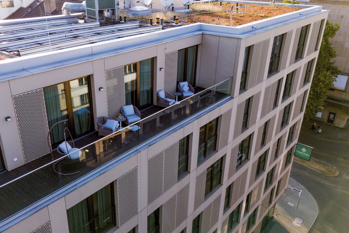 A modern building with a rooftop garden, large windows, and outdoor seating on the balcony.