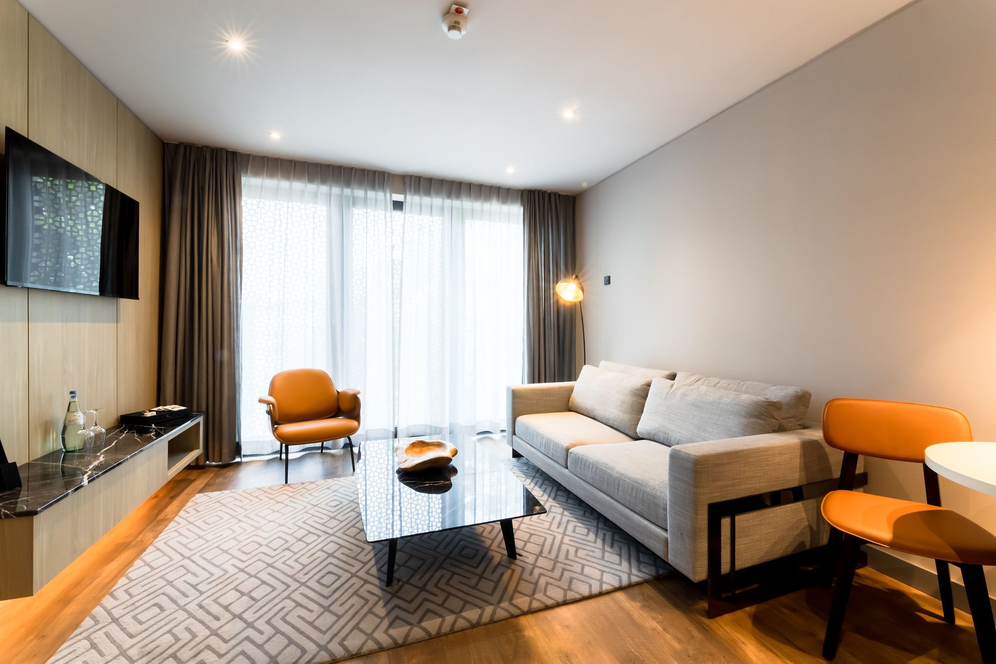 Ein modernes Wohnzimmer mit einer Couch, einem Couchtisch und zwei Sesseln. Ein Flachbildfernseher ist an der Wand montiert, und ein kleiner Tisch mit Glasplatte steht daneben.