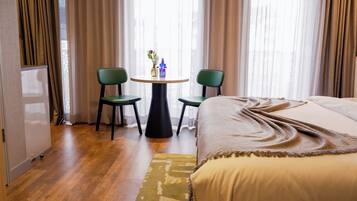 A hotel room with a bed, two chairs, a small table with a vase, and a window with curtains.