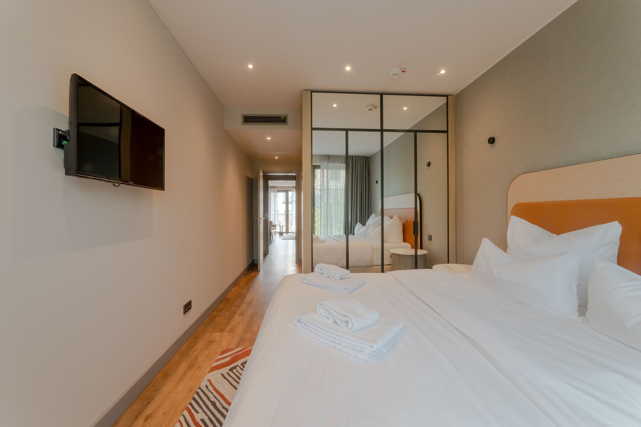 Une chambre d’hôtel dotée d’un grand lit, d’un téléviseur à écran plat fixé au mur, d’une porte-fenêtre coulissante donnant sur un balcon, et d’une salle de bain moderne avec douche et toilettes.