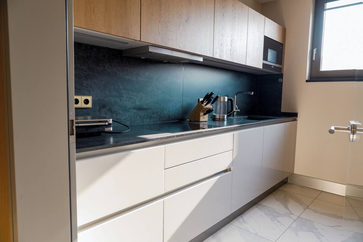 A modern kitchen with white cabinets, a black countertop, and a stainless steel kettle.