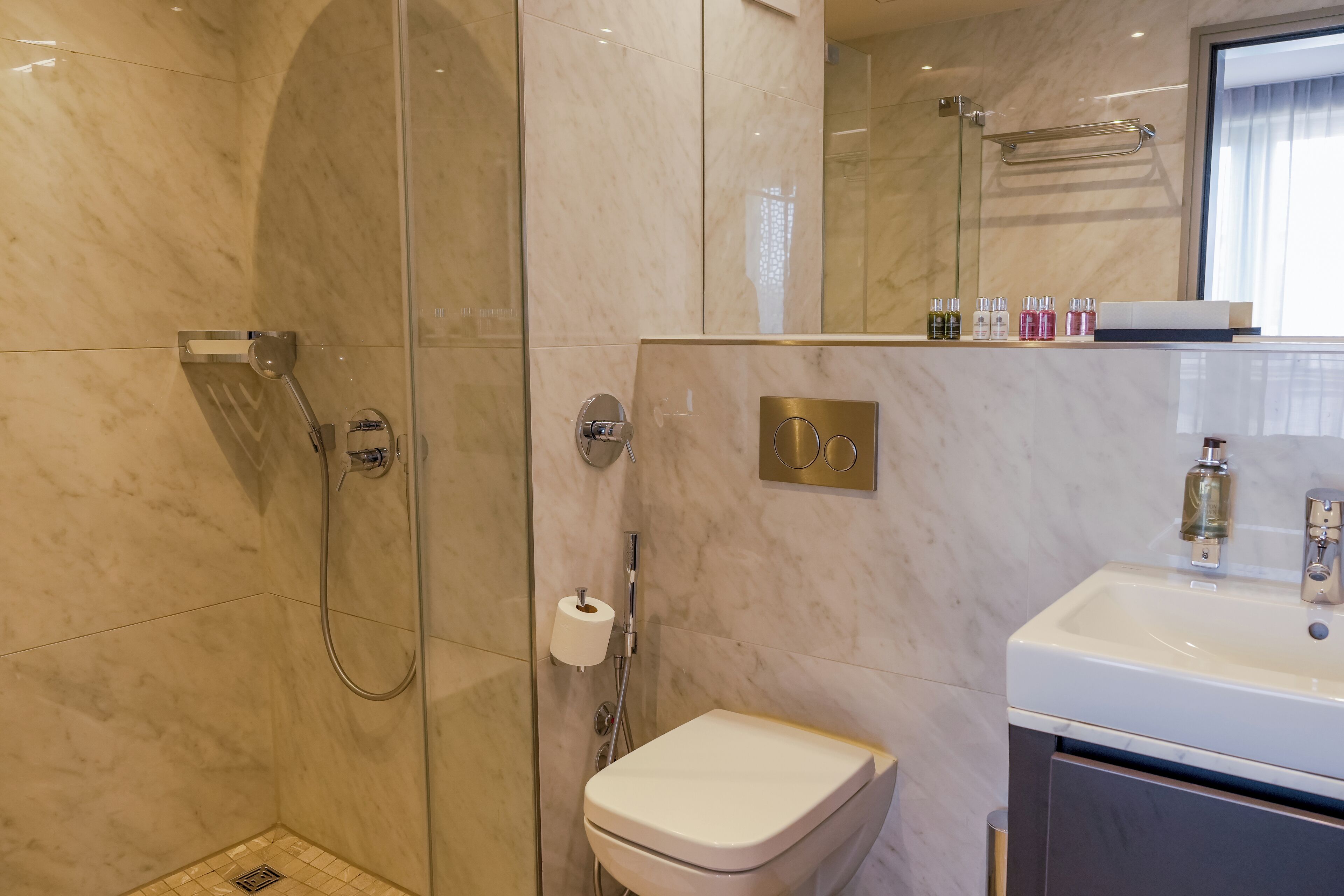 Een moderne badkamer met een douche met glazen wand, een toilet en een wastafel met toiletartikelen.