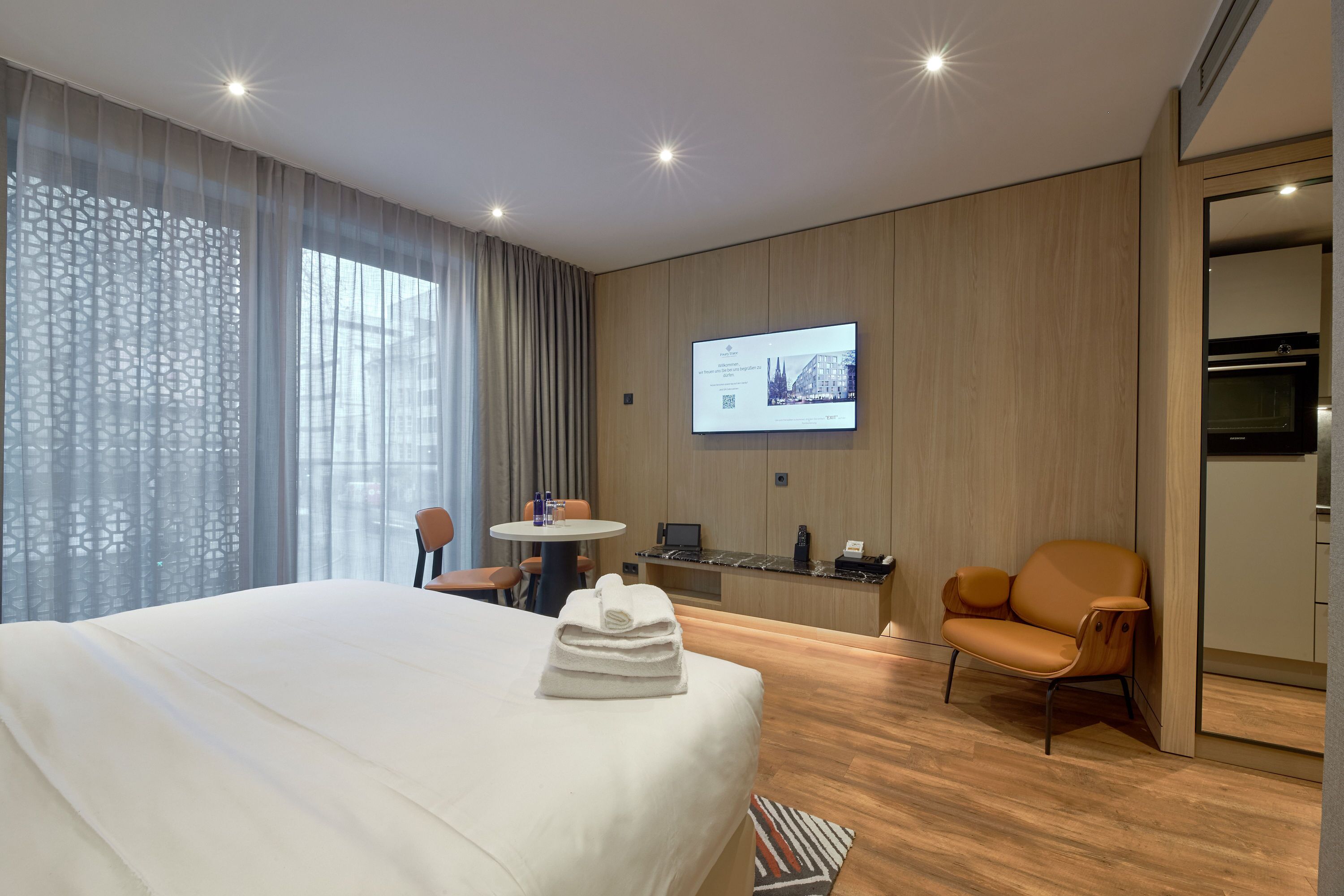 Una habitación de hotel moderna con una cama grande, un escritorio con una computadora portátil, una silla y un televisor en la pared.