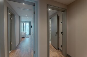 Un pasillo moderno con piso de madera, que conduce a una habitación con cama y ventana con cortinas.