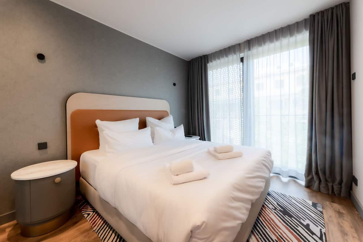 A modern hotel room with a large bed, a bedside table, and a window with curtains.