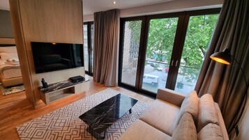 Una sala de estar moderna con un televisor de pantalla plana, un sofá, una mesa de centro y vistas a la calle a través de grandes ventanales.