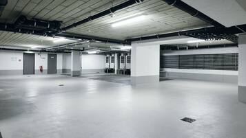 A spacious, well-lit parking garage with concrete floors and white walls, featuring multiple doors and a fire extinguisher.