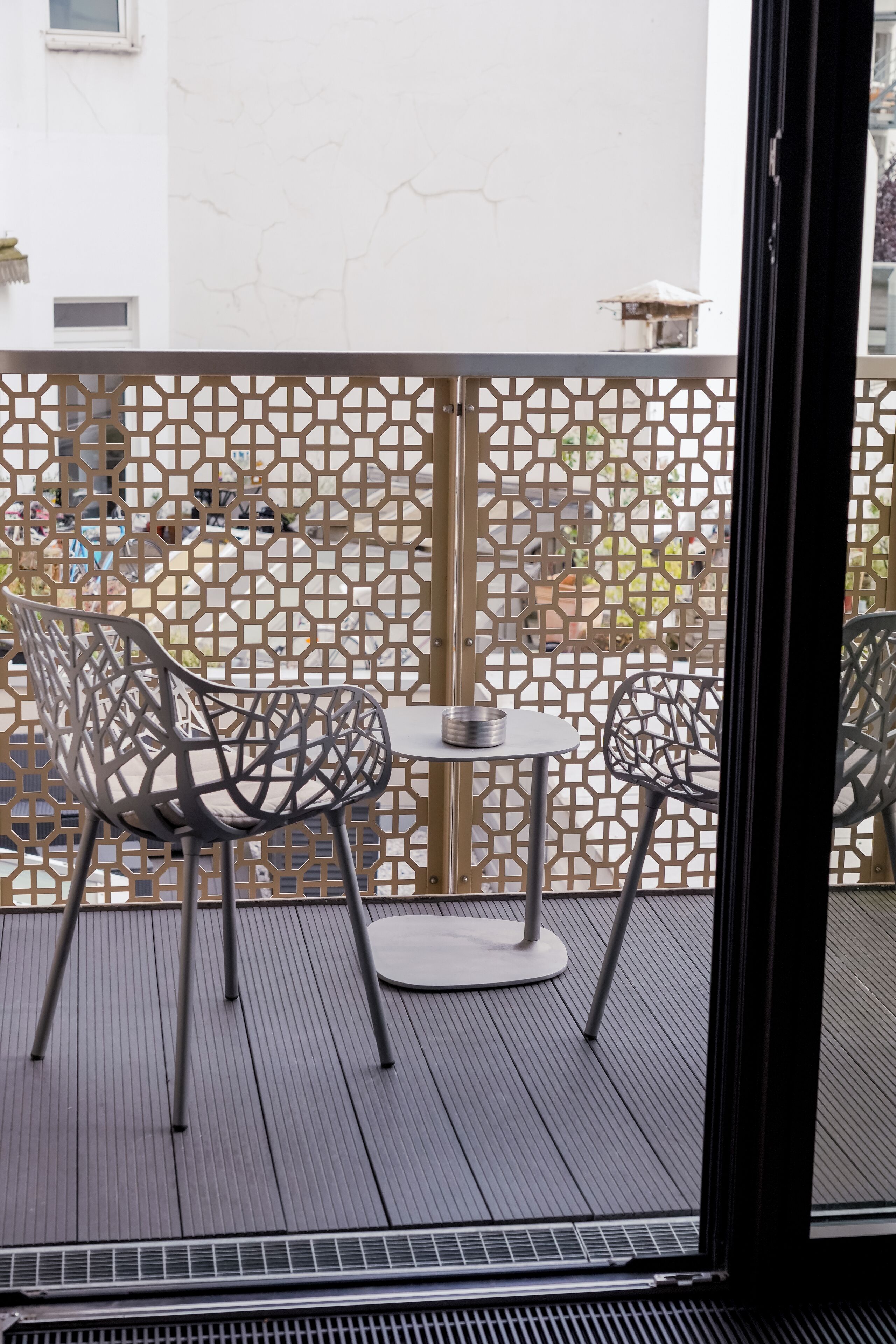 A balcony with two metal chairs and a small round table.