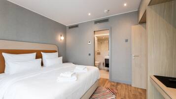 A modern hotel room with a large bed, a wooden wardrobe, and a bathroom visible through an open door.