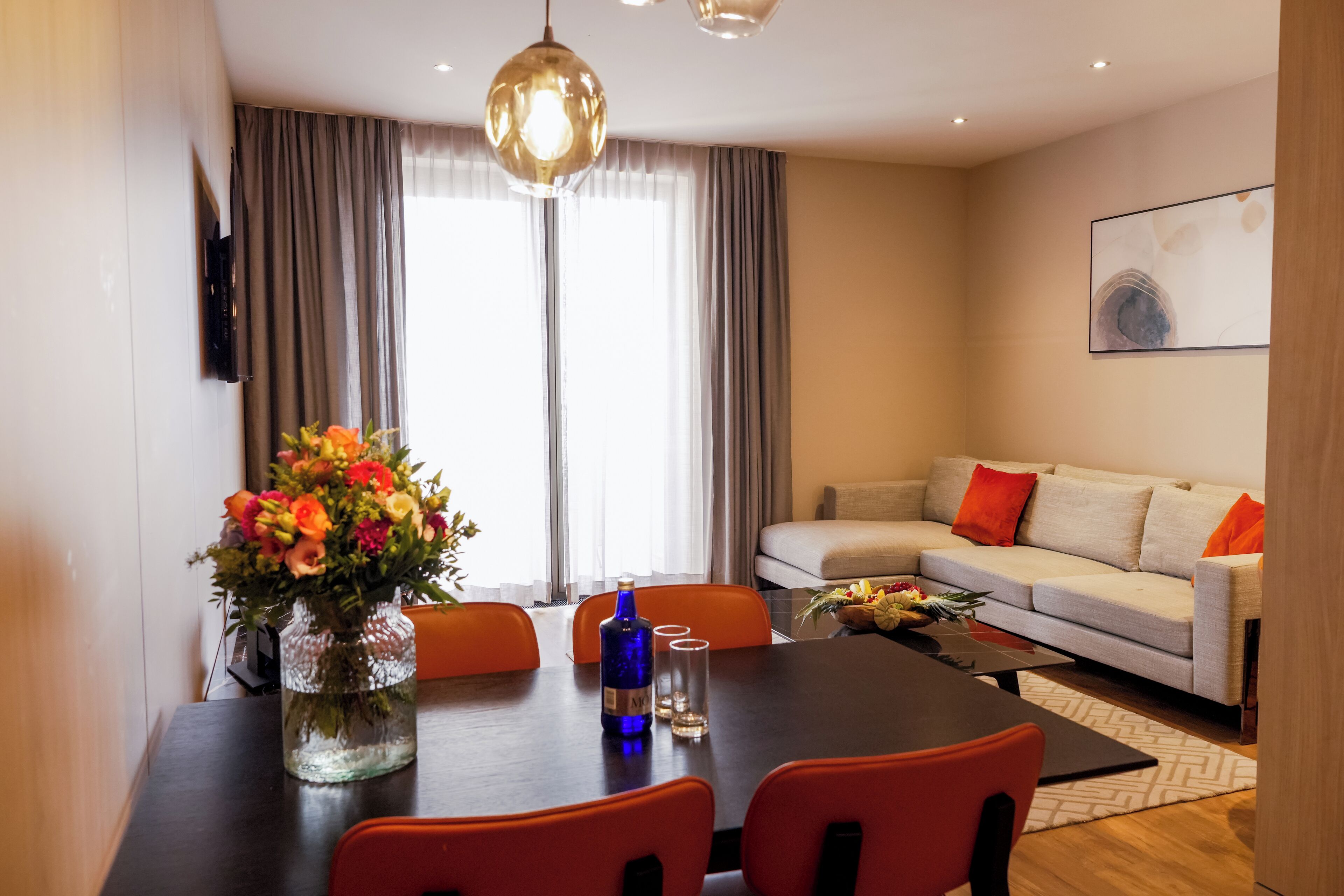 A modern living room with a dining table, chairs, a sofa, and a large window with curtains.