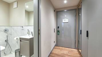 A modern bathroom with a shower, toilet, and sink, and a hallway leading to a door with a sign.