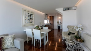 A modern living room with a dining area, a kitchen in the background, and a small side table with a plant.
