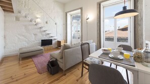 A modern living room with a staircase, a dining area with breakfast items, and a TV. - Cativo Mezzanine Studio by LovelyStay (Porto)