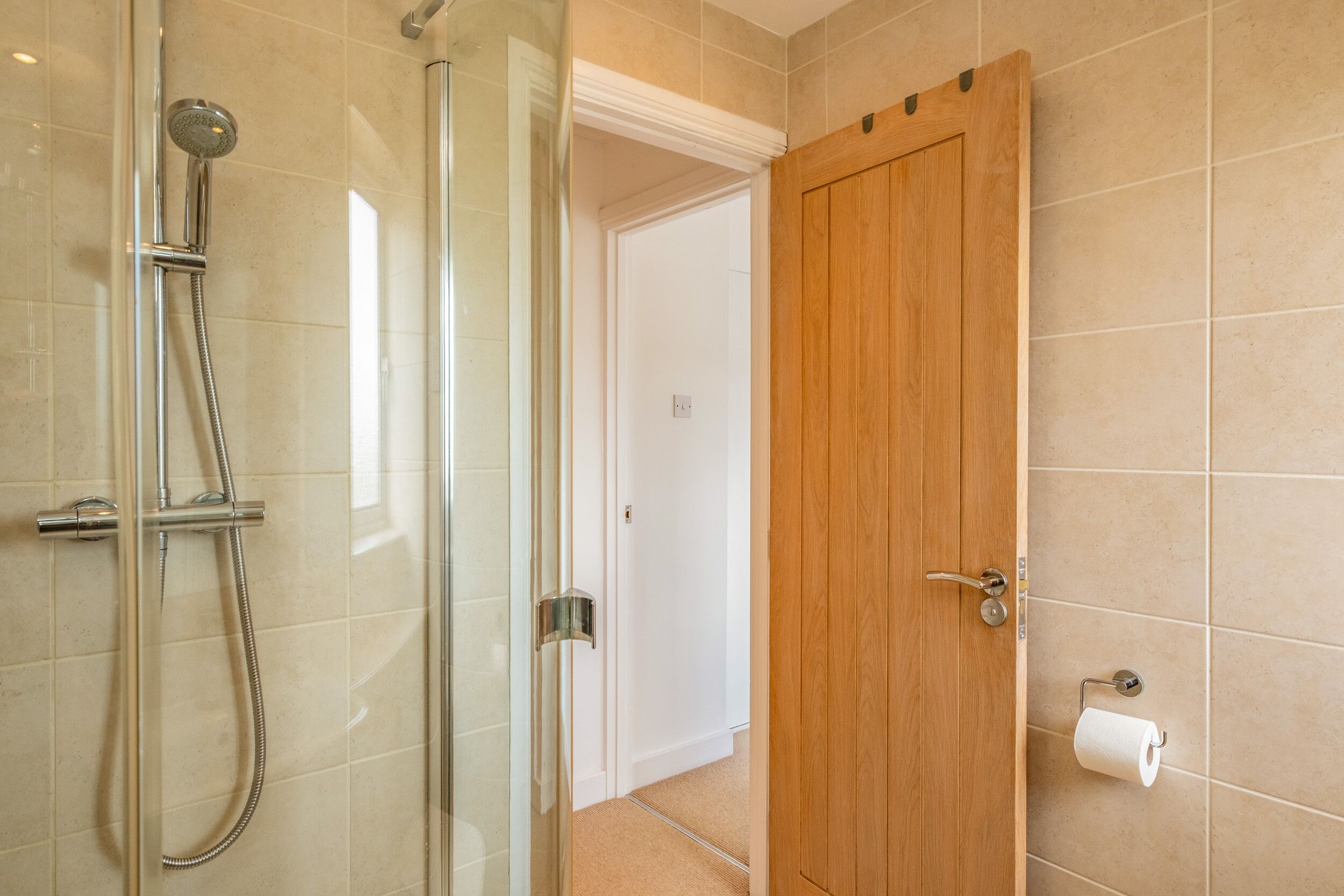 A bathroom with a glass shower enclosure, a wooden door, and a toilet paper holder on the wall.