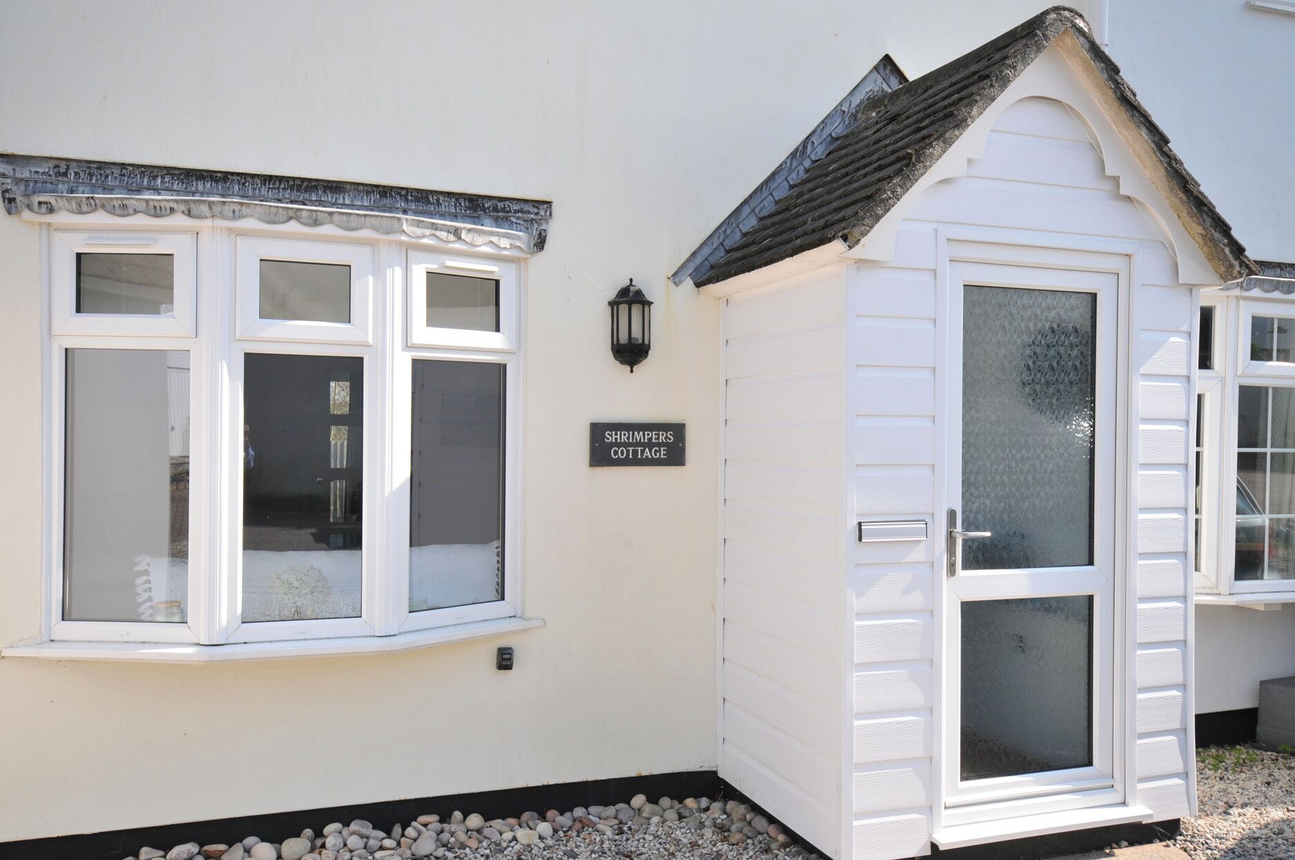 A white building with a sign reading 'SHRIMPERS COTTAGE,' a bay window, and a door with a glass panel.
