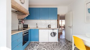 A compact kitchen with blue cabinets, a microwave, a coffee maker, and a washing machine.