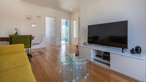 Een moderne woonkamer met een grote flatscreen-tv, een glazen salontafel en een gele bank.