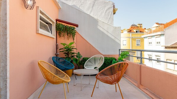 A balcony with wicker chairs, a small table, and potted plants.