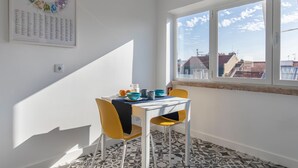 Een eetgedeelte met een tafel, stoelen en een raam met uitzicht op gebouwen.